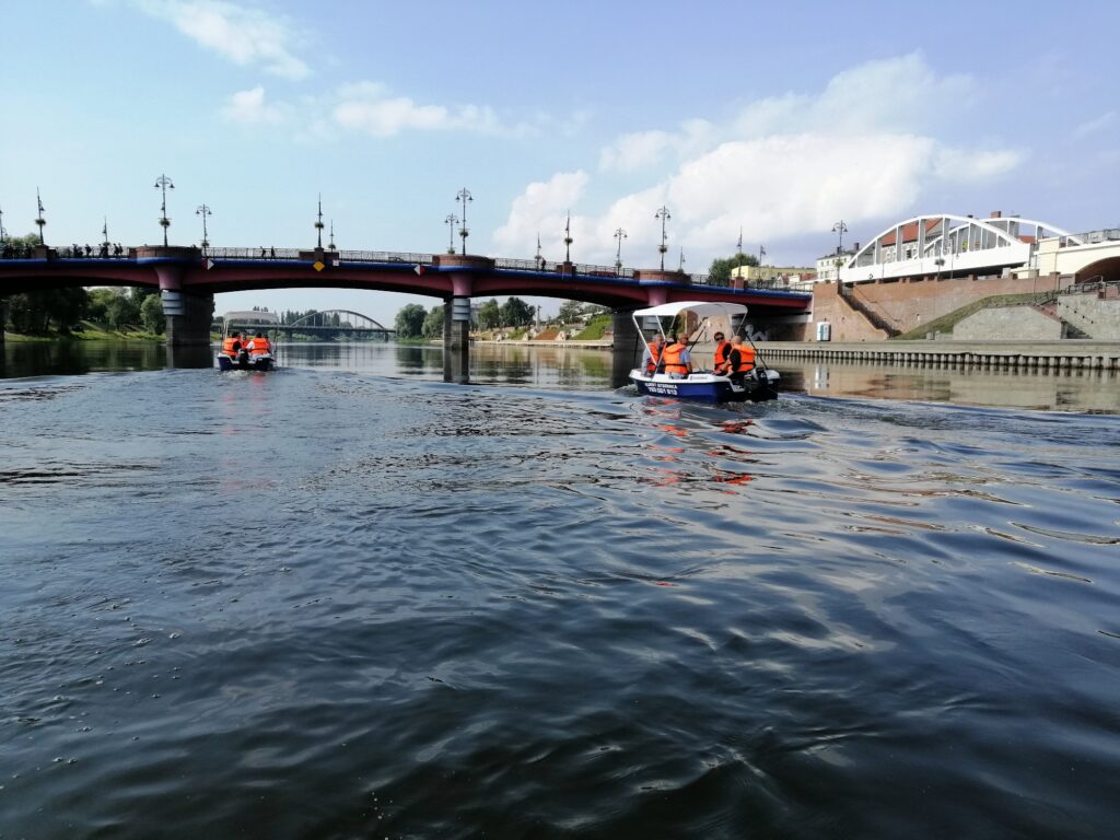 osoby na łodziach motorowych przepływających pod mostem